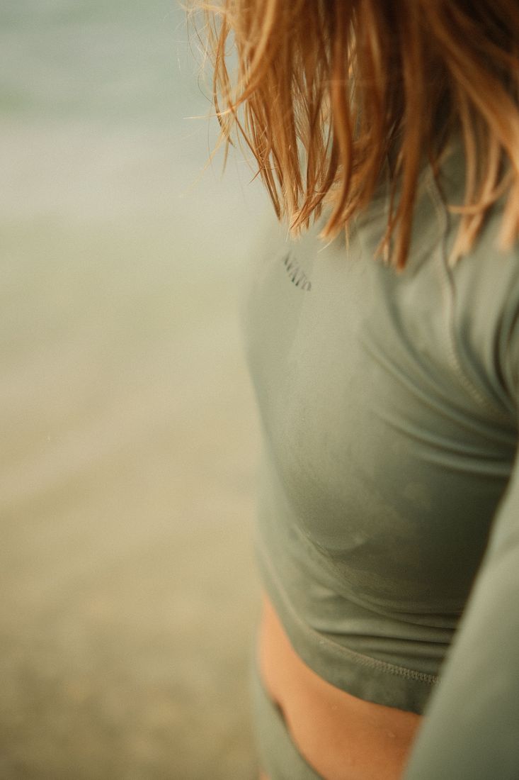 Close-up of a green long-sleeve surf top, hair blowing across it