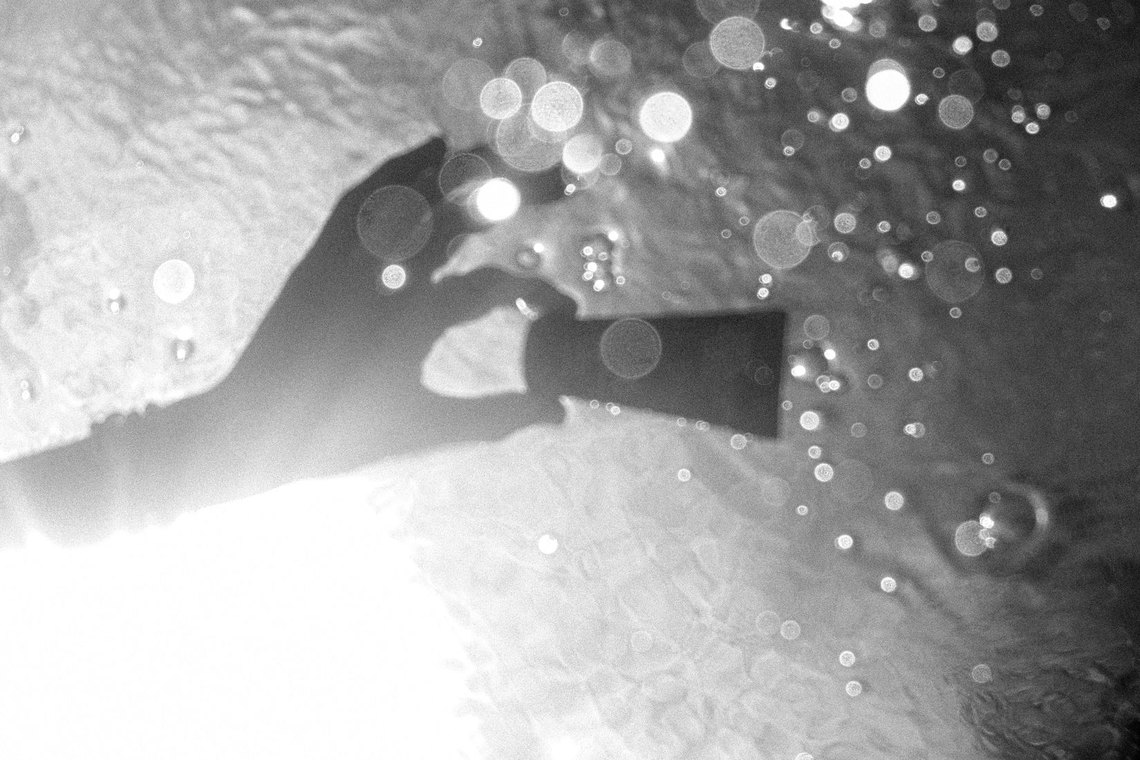 Black and white underwater shot of a hand holding a sunscreen tube among bubbles