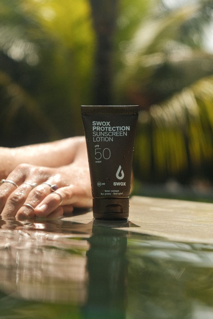 Swox SPF 50 tube standing on a pool edge, hands resting beside it, palms behind
