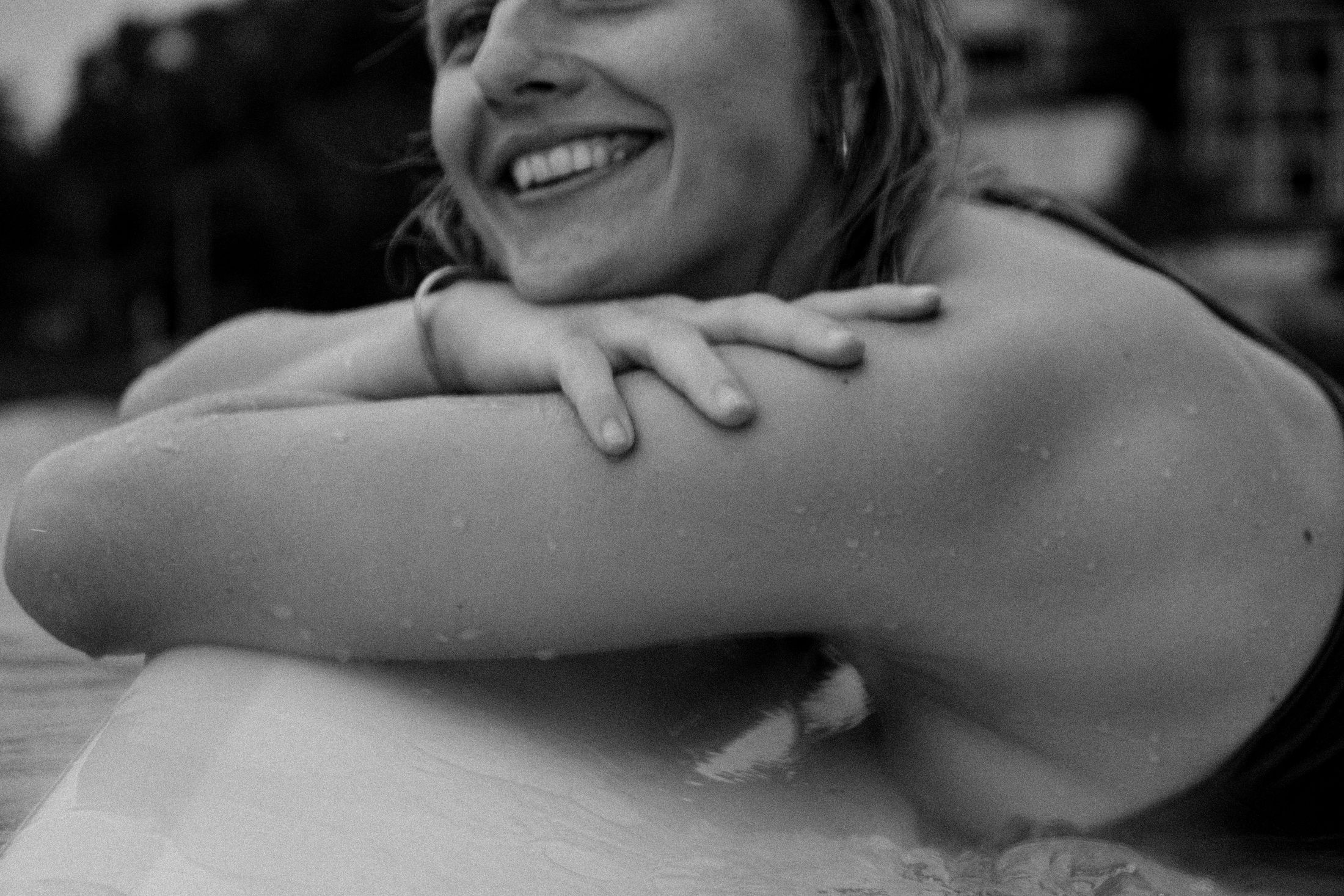 Black and white close-up of a woman laughing, arms folded over a surfboard