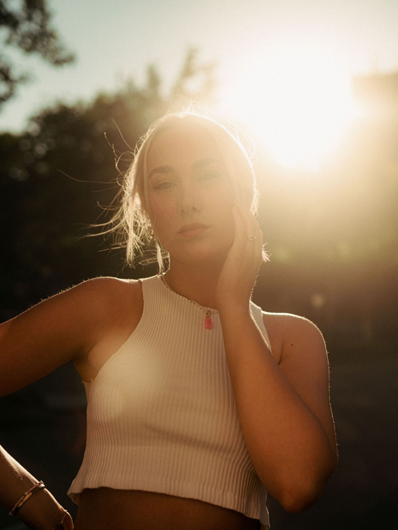 Woman in a white knit top in backlight, hand on her cheek