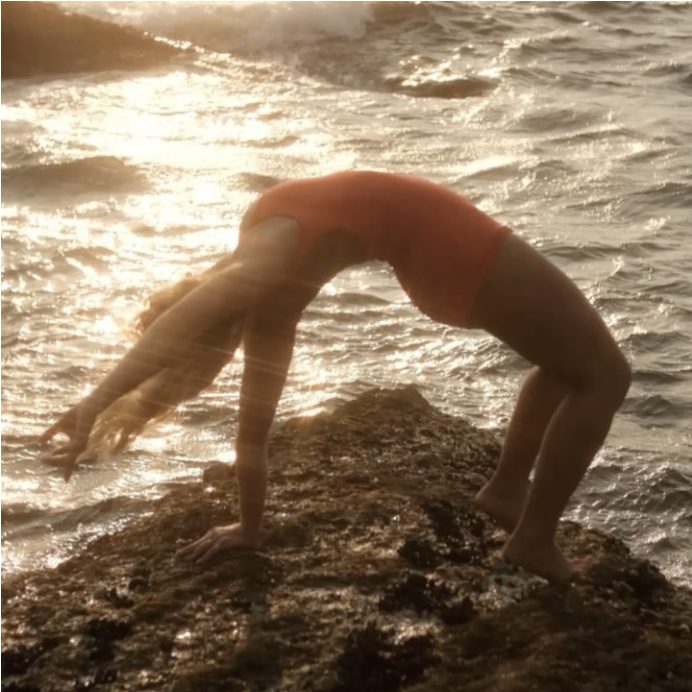 Woman in a backbend on a rock in sunlit shallow water