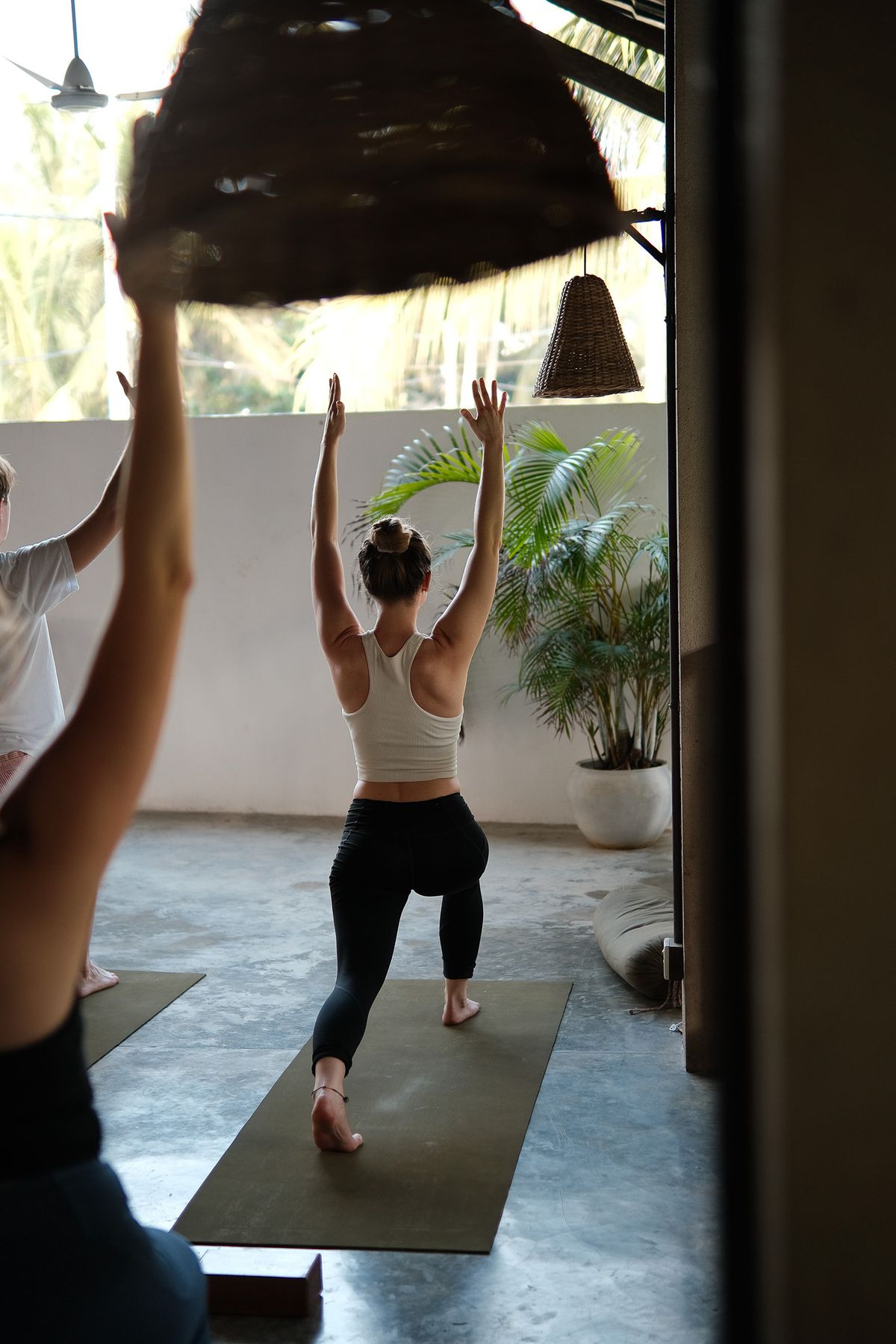 Woman in a high lunge with arms raised in the shala doorway