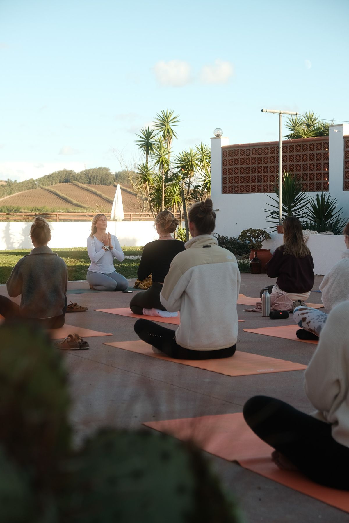 Yoga group sitting on mats on a lawn, hills behind