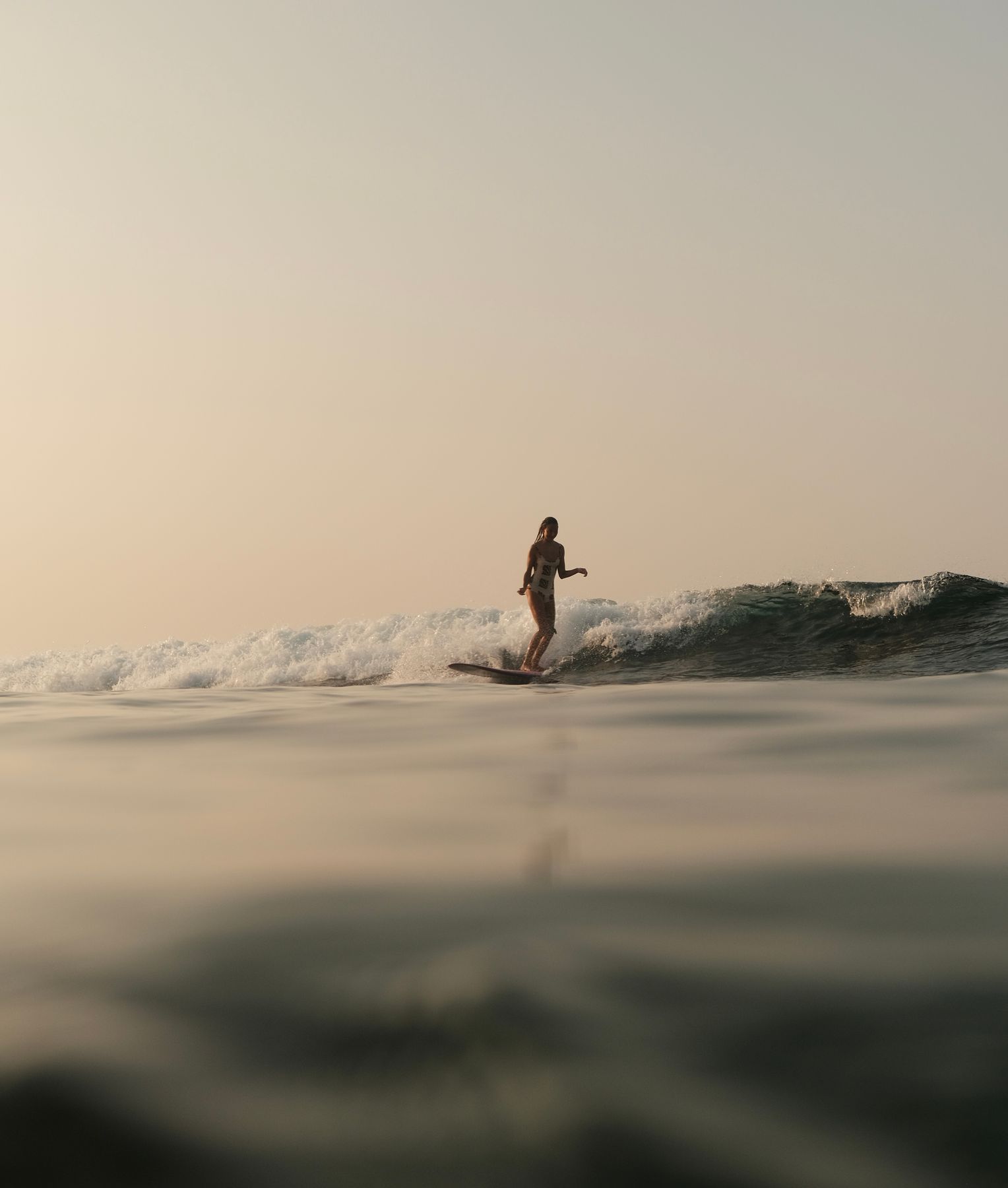 Woman riding a longboard on a small wave at sunrise, seen from water level