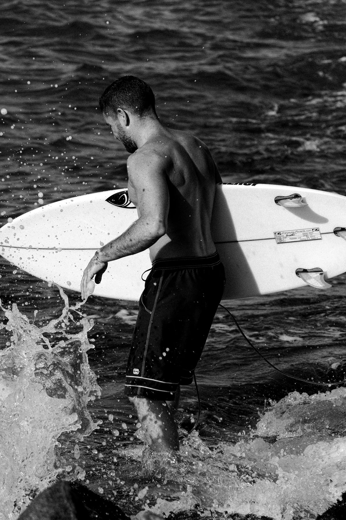 Black and white shot of a surfer climbing over rocks into the sea with his board