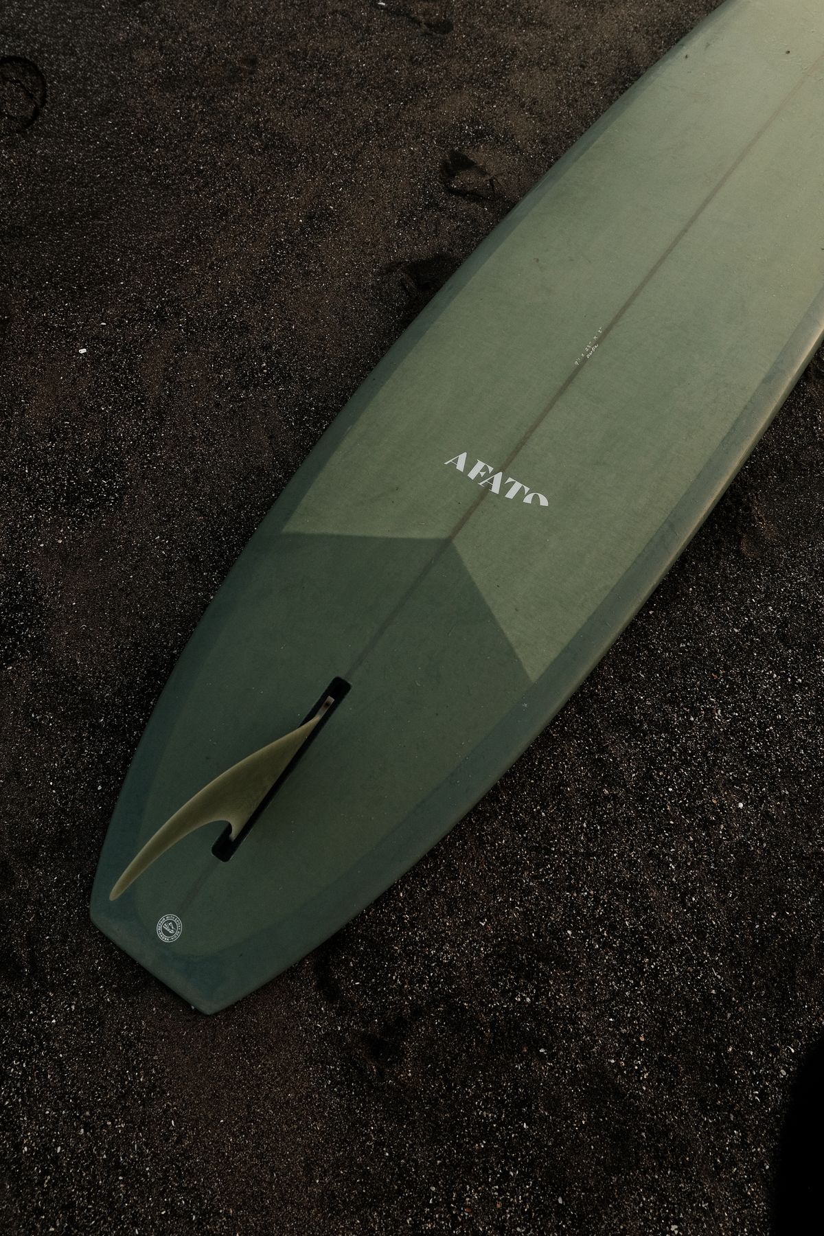 Sage green surfboard lying on dark sand, seen from above
