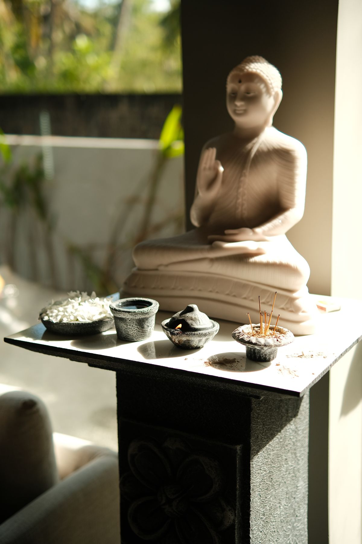 Stone Buddha statue on a dark plinth with offering bowls